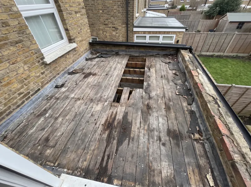 An old flat roof stripped back to weathered boards, with a section opened up to the joists